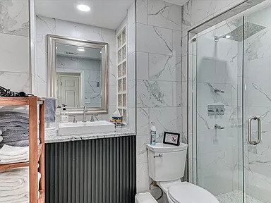 The Azalea bathroom with a marble-topped vanity, framed mirror, and glass-enclosed shower