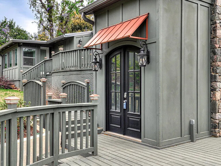 The large front-entrance deck at twilight — arched black doors lit by lanterns, azaleas in bloom, and warm under-deck lighting