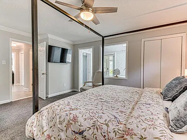 The Magnolia's second bedroom with an upholstered headboard and a view down the hall