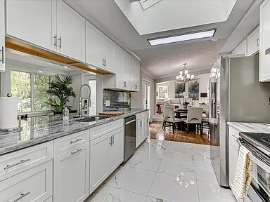 Renovated main-home kitchen with white cabinetry, grey marble counters and backsplash, and a stainless range