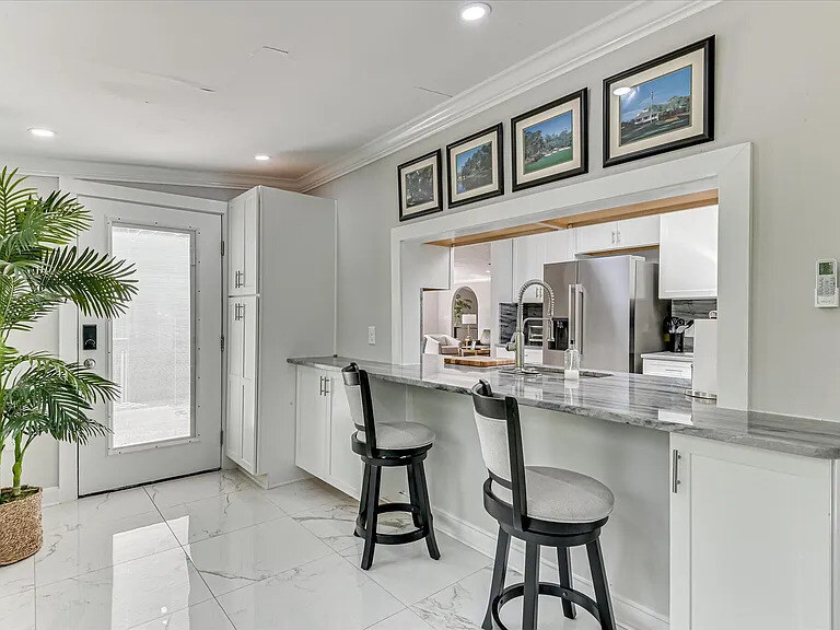 The marble counters and white cabinetry of the main kitchen at The Wilkshire House with the dining area visible beyond