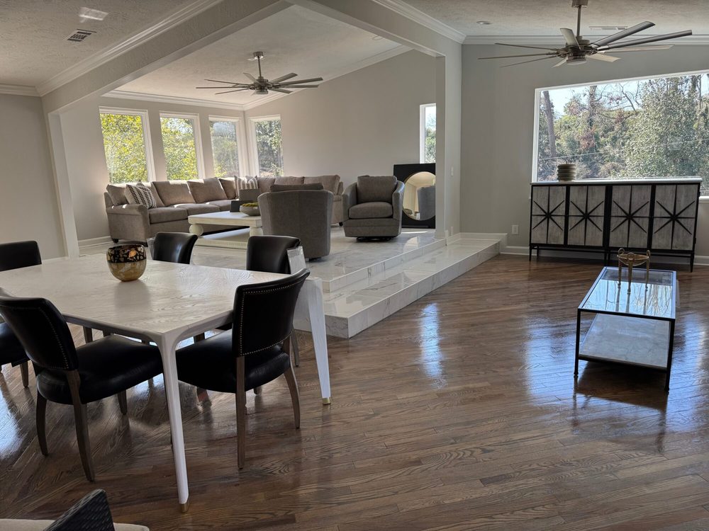 A grey sectional and accent chairs facing the dining table on the marble-tiled level of the main home