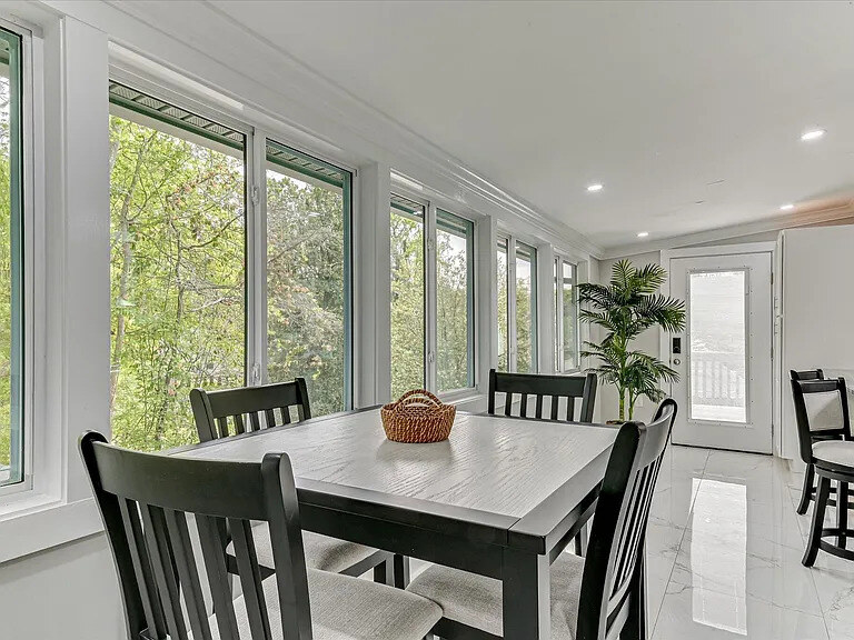 The Magnolia's breakfast-sunroom: navy woven armchairs, a round table, and a wall of windows onto the backyard